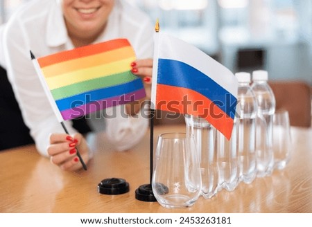 Young woman in business clothes puts flags of LGBT and Russia on negotiating table in office