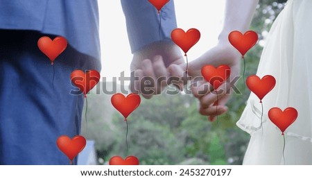 Image of multiple red heart balloons floating over mid section of newly married couple holding hands. Happy Valentines Day celebration concept digitally generated image. Royalty-Free Stock Photo #2453270197