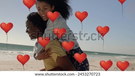 Image of red heart balloons floating over man giving piggyback ride to woman at beach. Happy Valentines Day celebration concept digitally generated image.