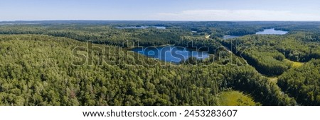Panoramic aerial view of a vast boreal forest with small blue lakes under a pale blue sky. A road runs through the forest.
