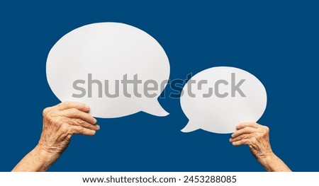 Close-up of a senior woman's hands holding a blank white speech bubble against a blue background. Space for text