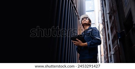 A man wearing a hard hat and safety glasses is holding a tablet in his hand. He is looking up at something, possibly a sign or a piece of equipment. Concept of focus and determination