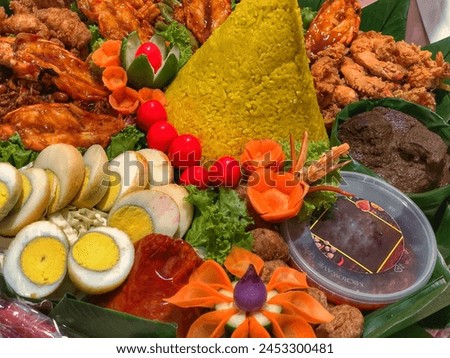 Yellow rice in a cone shape. In Indonesia called “Nasi Tumpeng” A festival Indonesian Rice dish with side dishes. Tumpeng rice in banana leaf and bamboo woven tray. Royalty-Free Stock Photo #2453300481