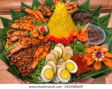 Yellow rice in a cone shape. In Indonesia called “Nasi Tumpeng” A festival Indonesian Rice dish with side dishes. Tumpeng rice in banana leaf and bamboo woven tray. Royalty-Free Stock Photo #2453300669