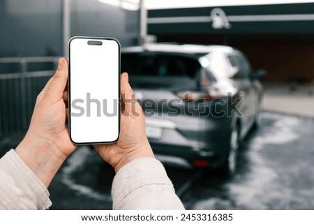 Hands with a blank phone screen on the background of a car wash.