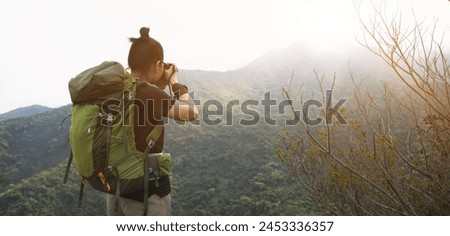 Woman photographer taking pictures on top of summer mountains