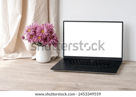 Luxury home interior decor and workspace, laptop computer blank display mock up, vase with pink daisy flowers on beige wooden table, white wall and linen curtain background with sunlight shadows.