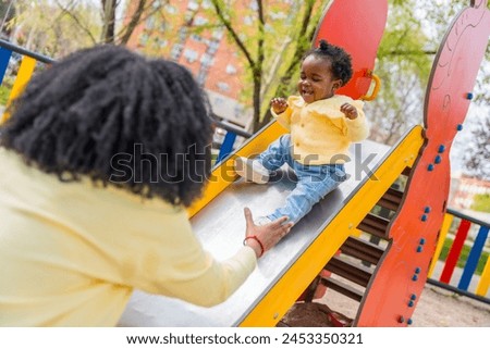 Happy african child playing with her mother in the slide in a public playground