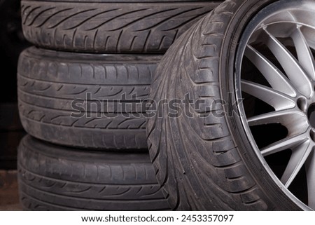 Automobile composition made up stack of tires and wheel with shiny disc in a car service before seasonal replacement or after breaking through. Royalty-Free Stock Photo #2453357097