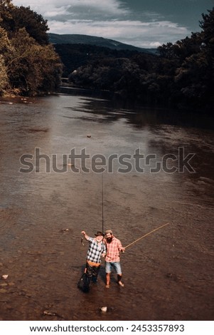 Two men friends fishing. Flyfishing angler makes cast, standing in river water. Old and young fisherman. Royalty-Free Stock Photo #2453357893