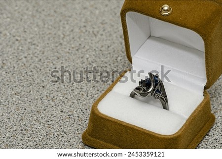 Ring in a jewelry box on background of light grey tile for texture and wallpaper