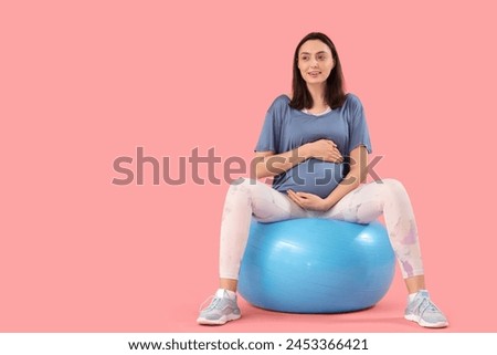 Beautiful young pregnant woman sitting on fitball against pink background