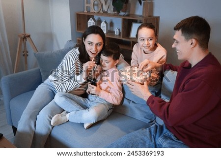 Happy family with popcorn and soda watching TV on sofa at home in evening