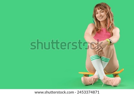 Young woman with skateboard sitting on green background