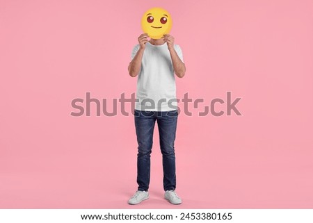 Man covering face with smiling emoticon on pink background