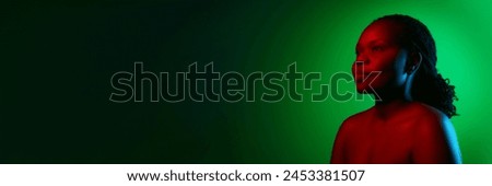Beautiful African woman with well-kept, spotless skin, posing on green studio background in neon light. Concept of natural beauty, ethnicity, self-care, wellness, positive emotions. Banner Royalty-Free Stock Photo #2453381507