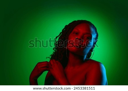 Elegant African woman with bare shoulders, well-kept spotless skin, posing on green studio background in neon light. Concept of natural beauty, ethnicity, self-care, wellness, positive emotions Royalty-Free Stock Photo #2453381511