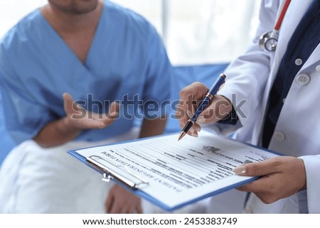 Professional female doctor with stethoscope around her neck talks with male patient, asks patient to fill out form, patient history, disease symptoms, body aches to plan treatment at hospital bed.