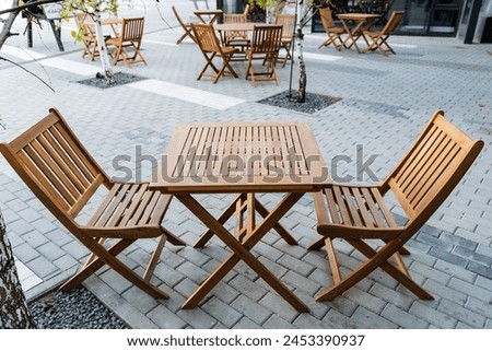 Outdoor furniture set including a wooden table and chairs, placed on a brick sidewalk. The furniture is made of natural material with a wood stain finish