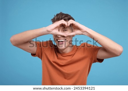 Happy man showing heart gesture with hands on light blue background
