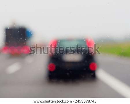 A blurry image of a busy street with cars and a truck. The rain is making the windshield of the cars and truck wet