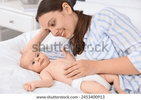 Happy young woman applying body cream onto baby`s skin on bed