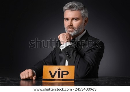 Handsome man sitting at table with VIP sign on black background