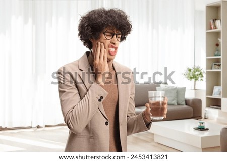 Young man with hypersensitive teeth holding a glass of water at home Royalty-Free Stock Photo #2453413821