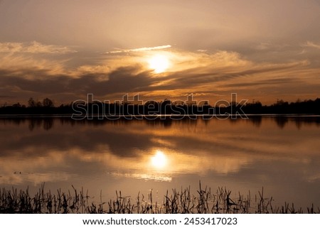 The sky and the lake are red-tinged during sunset, a beautiful sunset on the lake in early spring Royalty-Free Stock Photo #2453417023