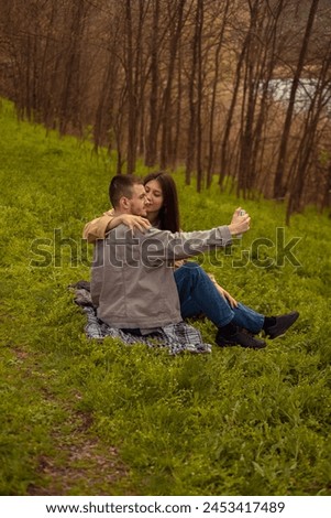 A guy and a girl take a selfie on their phone during a picnic in the forest, capturing a romantic date in nature.