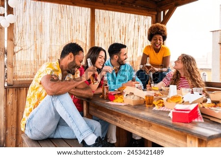 Multiethnic group of happy young friends having dinner barbecue party on rooftop at home - Multiracial cheerful young adult people having fun and bonding on a terrace balcony with city view