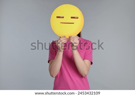 Woman holding emoticon with closed eyes and mouth on grey background