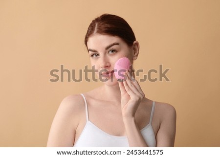 Washing face. Young woman with cleansing brush on beige background