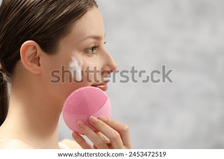 Young woman washing face with brush and cleansing foam indoors, closeup. Space for text