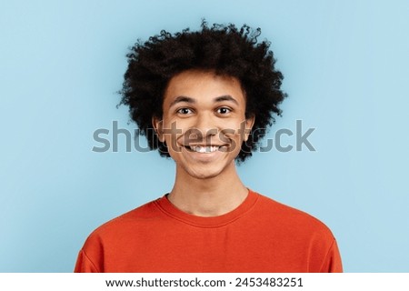 Portrait of a joyful african american guy with an engaging smile, wearing an orange sweater, posed against a blue isolated background. Depicts happiness and youthfulness Royalty-Free Stock Photo #2453483251