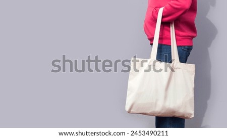 Woman in red hoodie holding tote canvas blank eco bag on street grey minimal wall background. Female consumer hold white textile shopper. template or place for your design, logo, text