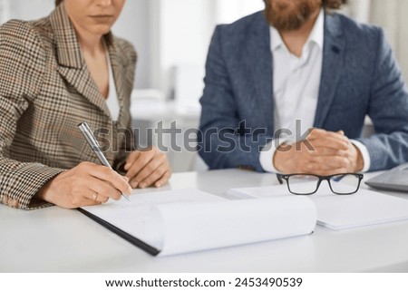 Signing of business contract. Woman in office signs paper document confirming purchase of house or loan from bank. Serious female client sitting near agent signs document. Selective focus.