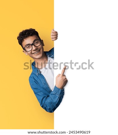Excited young man wear eye glasses, braces, stand behind, peep from blank empty banner mockup sign board signboard, advertise show area for sales slogan text, isolate yellow background. Dental care ad