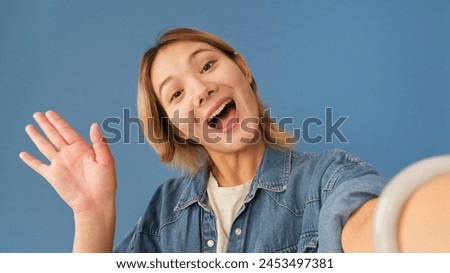 Close-up of young woman looking at camera making video call, welcome sign, isolated on blue background