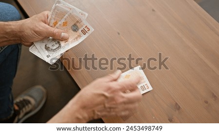 Man exchanges british pounds on a wooden table, depicting a transaction or payment indoors.