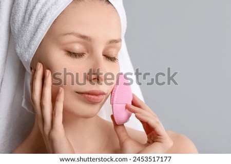 Washing face. Young woman with cleansing brush on grey background, closeup. Space for text