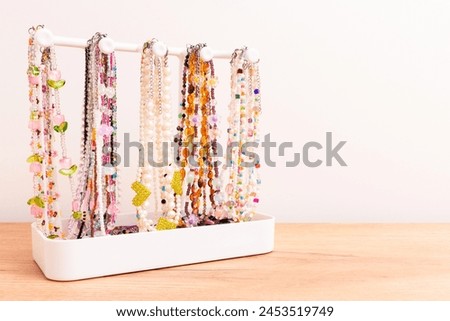 Various handcraft chains of beads, pearls and natural stones hanging on a stand in front of beige background. Trendy accessories.