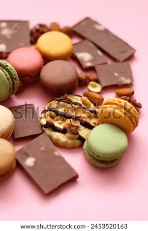Pastel macarons, almond chocolate, peanut butter cookies and various nuts on bright pink background. Selective focus.
