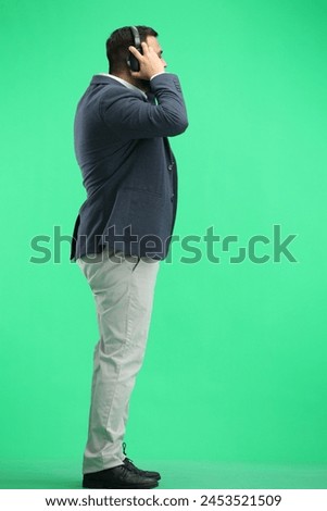 A man, full-length, on a green background, listening to music with headphones