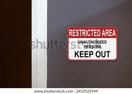 Red and white restricted area sign on the side of a corridor stating : Restricted Area, Unauthorized persons keep out.