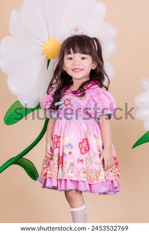 Portrait asia girl in pastel pink skirt . Shot in a studio with a orange background. And there is a flower prop on the back. She poses cutely and is in a good mood.