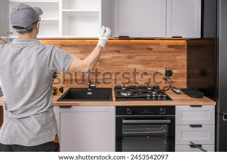 Caucasian Cabinetmaker in His 40s Finishing Kitchen Cabinets Installation. Modern White and Elegant Kitchen Design. Royalty-Free Stock Photo #2453542097