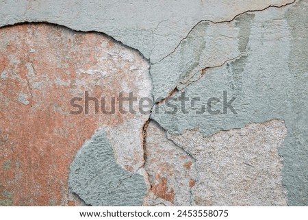 Colorful green-orange-yellow wall surface of an old building with crumbling plaster, cracks and stains as a textured background. Copy space. Selective focus. Royalty-Free Stock Photo #2453558075