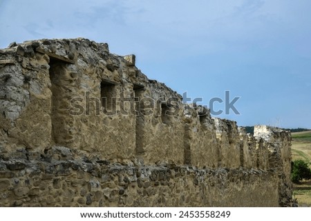 Wall of ancient Rupea fortress with loopholes in Romania against blue sky with clouds. Fortress was built on ruins of former Dacian defensive structure. Copy space. Selective focus. Royalty-Free Stock Photo #2453558249