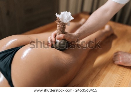Top view of Herbal Ayurvedic massage with Kizhi Herbal Bags on buttocks. Relaxed female client receiving herbal bolus bags massage. Tranquil and serenity of aromatherapy recreation at spa salon. Royalty-Free Stock Photo #2453563415